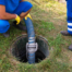 Two workers pumping household septic tank underground with blue pipe