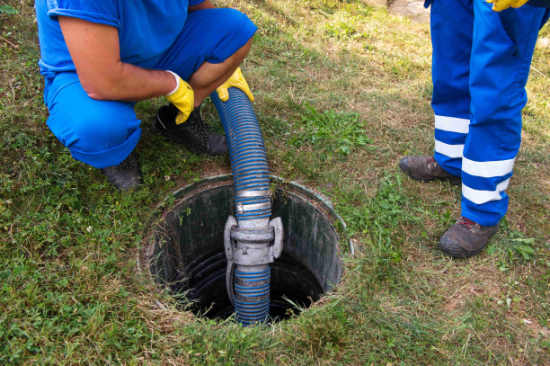 Two workers pumping household septic tank underground with blue pipe