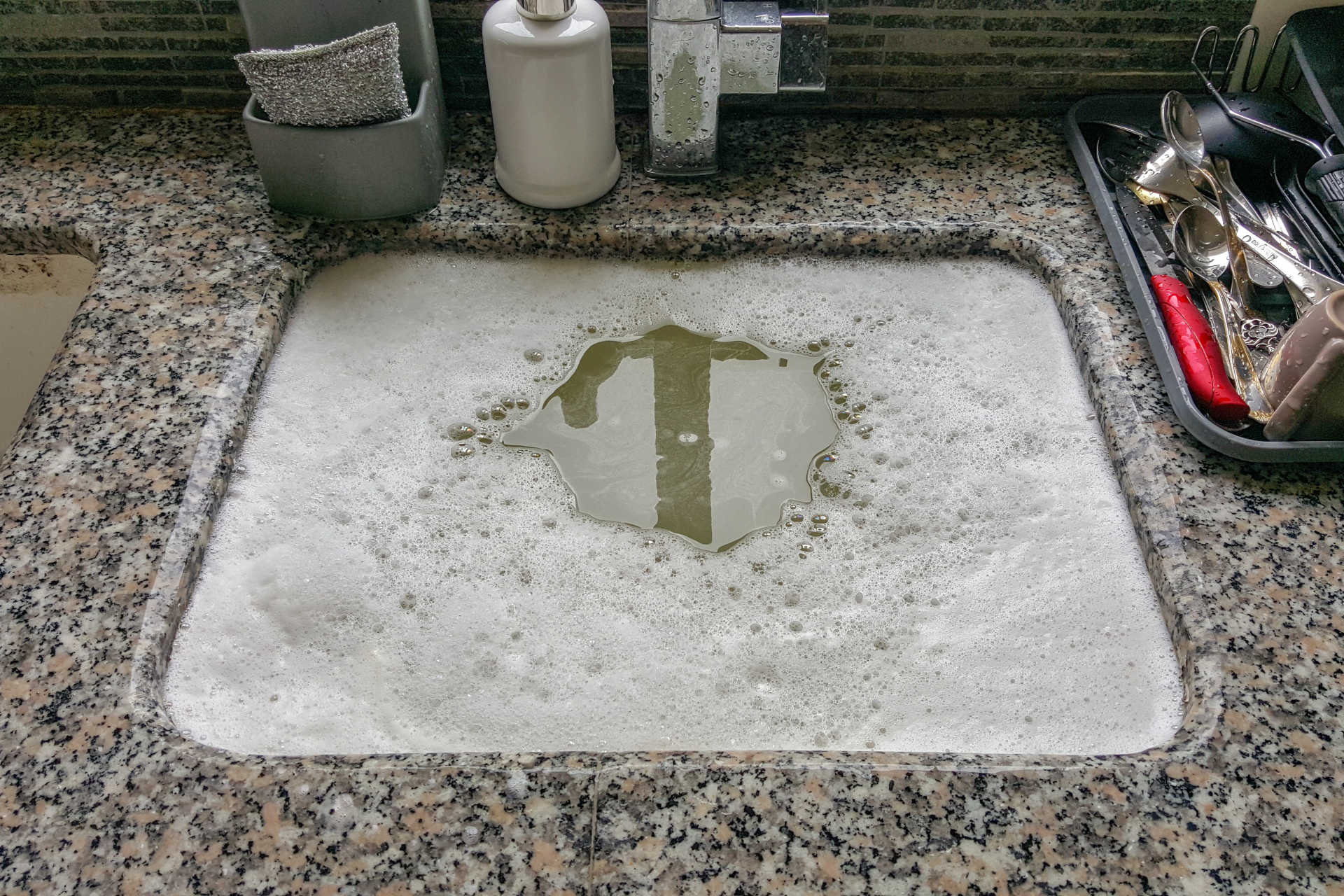 Kitchen sink with blocked drain, full of dirty dishwater.